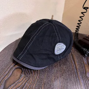 Close-up of black retro flat cap with gray contrast stitching and vintage side patch logo