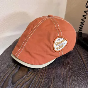 Detail of vintage terracotta newsboy cap with white stitching and embroidered side patch