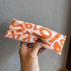 Close-up of pink and orange knitted headband featuring intricate geometric logo patterns