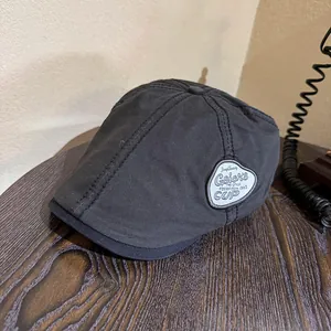 Detail of charcoal black newsboy cap featuring a stitched decorative vintage patch