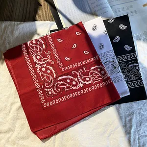 Trois bandanas paisley en rouge, blanc et noir empilés sur un fond texturé élégant