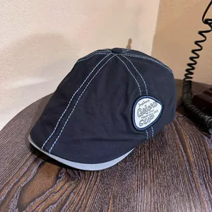Detailed close-up of a vintage navy flat cap with blue stitching and embroidery on wood