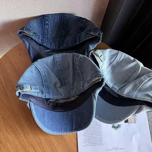 Three denim flat caps in varied blue washes on a wooden table with brass side buckles