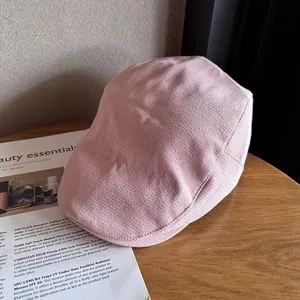 Detail of light pink knitted newsboy hat on a wooden table with fashion magazines