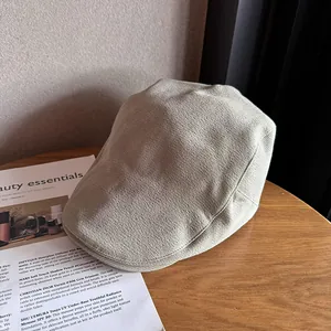Detail view of the fine woven texture on a beige knit flat cap on a wooden table