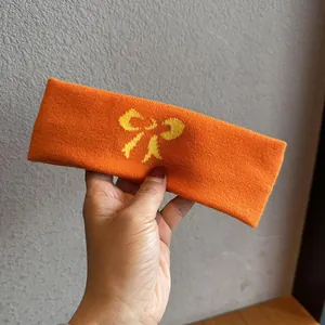 Detail eines orangefarbenen Strickstirnbands mit gelber Schleife und weicher Wollmischung