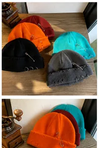 Detail of knit beanie featuring metal rings and pin decorations with distressed holes