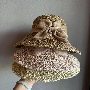 Detail of three folded straw hats in beige, pink and yellow with ribbon bows