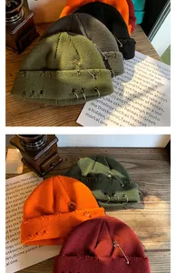 Close-up of distressed knit beanies with metal rings and pins on a wooden surface