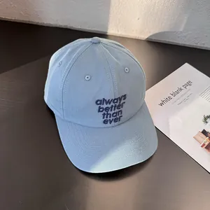 Detail of light blue cotton baseball cap featuring dark blue slogan embroidery on fabric