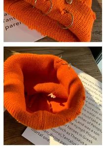 Detail of orange knitted beanie featuring silver rings and trendy distressed rip design