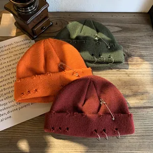 Three distressed knit beanies with metal rings and pins shown on a rustic wooden desk