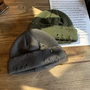 Hip hop knit beanie with metal rings and safety pins on a wooden surface
