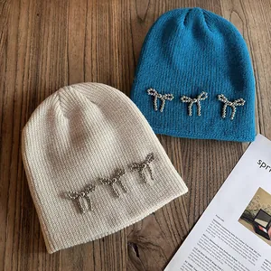 Bonnets en maille chic crème et bleu avec détails de nœuds perlés sur fond de bois