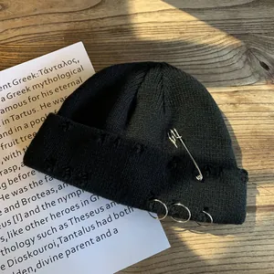 Black ribbed knit beanie with silver rings and safety pin on a rustic wooden background