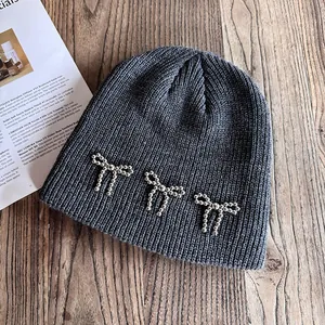 Détail du bonnet en maille gris foncé avec nœuds en perles argentées sur fond bois