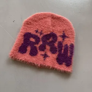 Detailansicht der flauschigen Plüschtextur und lila Buchstaben auf der rosa Strickmütze