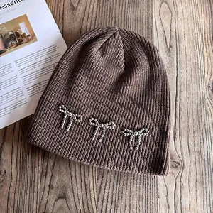 Détail du bonnet en maille marron foncé orné de nœuds en perles argentées sur bois