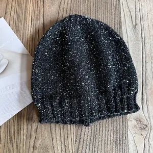 Sparkly black knit beanie with silver sequins and ribbed cuff on a wooden background