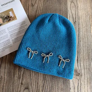Détail de bonnet en maille bleu vif avec trois nœuds décoratifs en perles argentées