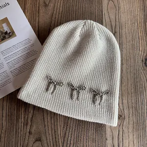 Détail du bonnet en maille crème avec nœuds en perles argentées sur fond de bois sombre