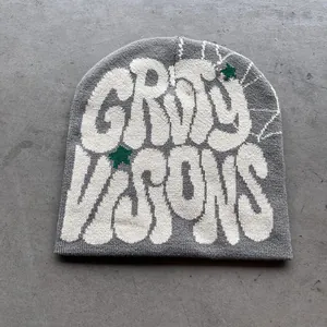 Detail van grijze gebreide muts met witte graffiti letters en groene sterren