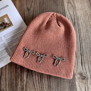 Détail du bonnet en tricot orange avec trois nœuds décoratifs en perles argentées