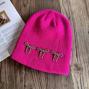 Détail du bonnet en maille côtelée rose avec nœuds perlés argentés sur bois