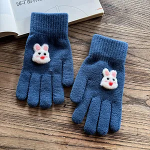 Detail of navy knit gloves with 3D white bunny plush and ribbed cuffs on wood background