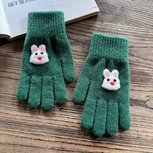 Close-up of green knitted gloves with cute 3D bunny decor and ribbed cuffs on wood