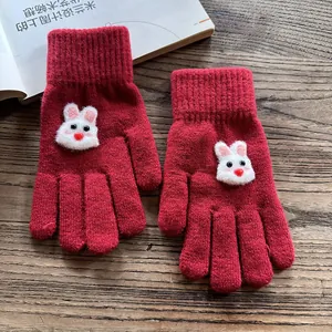Close-up of red knit gloves featuring cute 3D bunny patches on a wooden tabletop