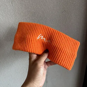 Details des orangefarbenen Rippstrick-Sport-Stirnbands mit weißer me Buchstaben-Stickerei