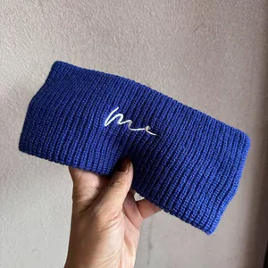 Detail eines dunkelblauen Strick-Stirnbands mit weißer 'me'-Stickerei aus Wolle