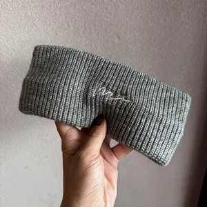 Nahaufnahme des grauen Strickstirnbands mit weißer Stickerei auf grobem Wollmaterial