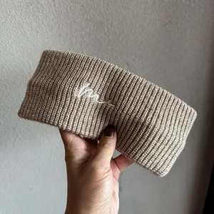 Detailansicht des khakifarbenen Strickstirnbandes mit weißem besticktem Buchstaben M