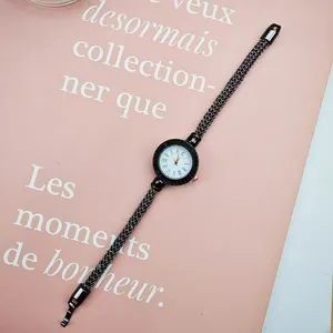 Detail of quartz watch with black mesh strap and rhinestone bezel on pink background