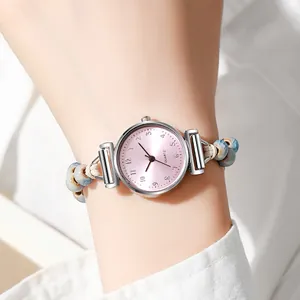 Detalle de reloj de cuarzo con esfera rosa, cuentas de cerámica azul y correa tejida