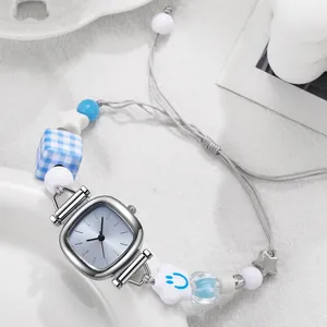 Detail of a square quartz watch with a blue beaded bracelet band on a ceramic tray