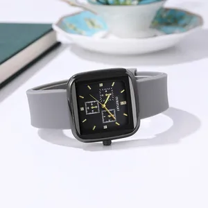 Close-up of square black watch dial with gold markers and grey silicone strap