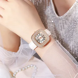 Détail d'une montre carrée en or rose avec lunette en cristal et bracelet en cuir blanc