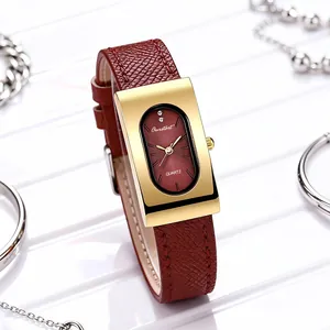 Close-up of a vintage rectangular gold watch with a deep red dial and leather strap