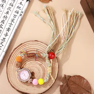 Detail der Boho-Webuhr mit Strasssteinen und bunten Pompons auf einem Holztablett