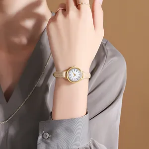 Close-up of minimalist gold watch with Roman numerals and beige leather strap on wrist