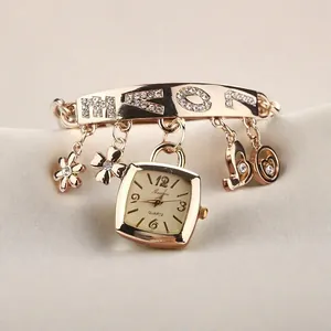 Détail de la montre bracelet dorée avec pendentif LOVE, fleurs en strass et cadran carré