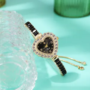 Dettaglio orologio a cuore dorato con ghiera di strass e quadrante nero su sfondo verde