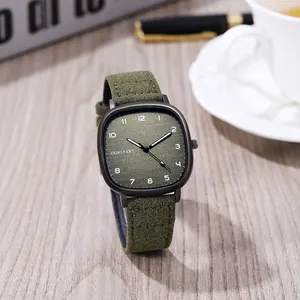 Close-up of green square quartz watch with matte case and suede strap on a wooden desk