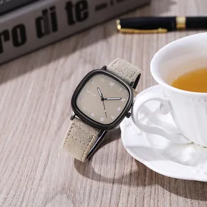 Macro shot of cushion quartz watch with khaki matte dial and suede strap on a desk