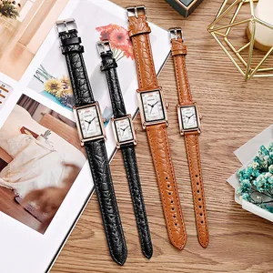 Matching rectangular quartz watches with brown leather straps on a wooden table setup