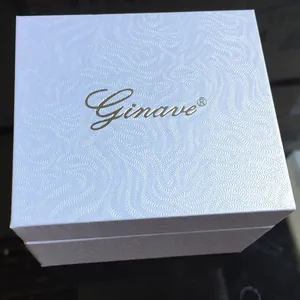 Detalle de caja blanca para reloj con textura de ondas y logotipo dorado fino