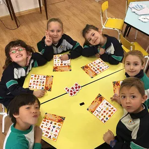 Children playing Thanksgiving bingo game cards with autumn leaf markers at a yellow table